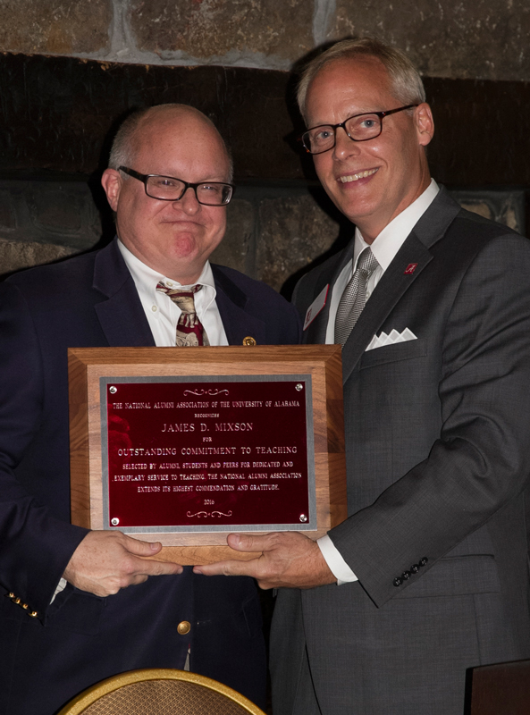 Photo of James Mixson receiving plaque for unknown individual. They are standing in front of a stone fireplace.