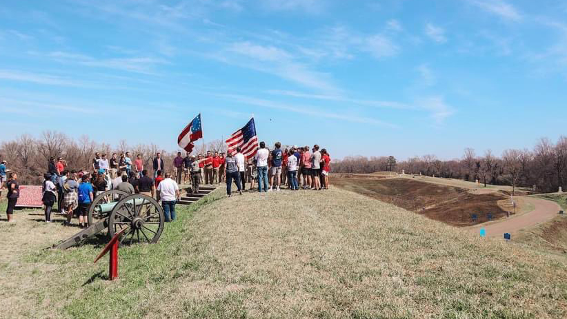 Students standing atop breastworks at Vicksburg with the First National Confederate Flag and the US Flag flying in background.
