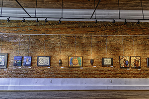 Brick wall inside Paul Jones Gallery showing a display of paintings and other artwork.