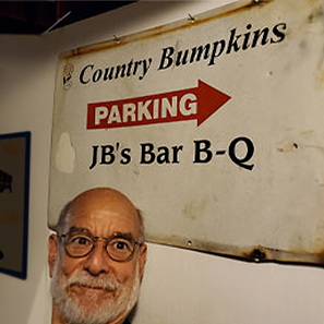 John Beeler in front of a sign advertising Country Bumpkins parking for JB's Bar B-Q.