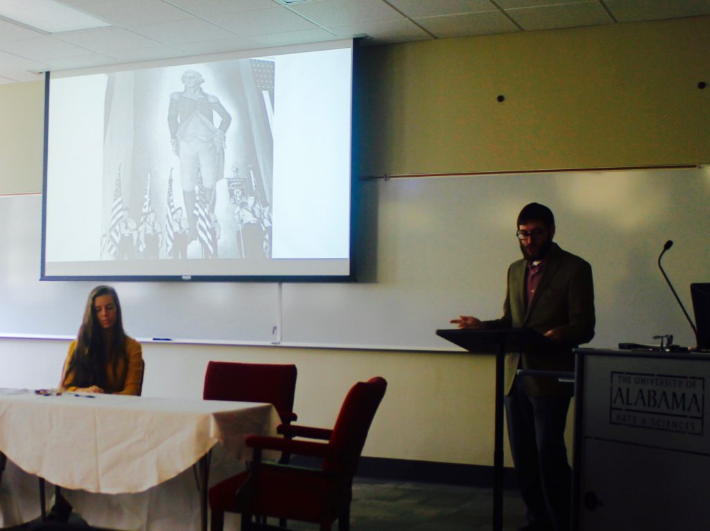 This image shows a panel presenter speaking in a ten Hoor classroom and another attendee sitting at a table.