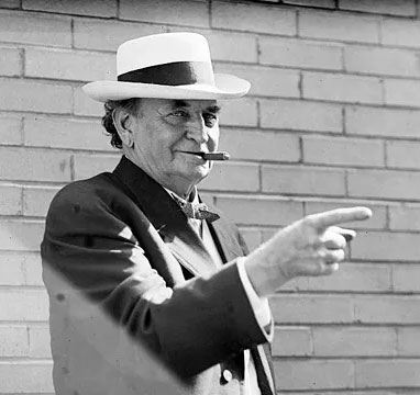 John H. Bankhead I in front of a brick wall, wearing a hat, smoking a cigar, and pointing a finger