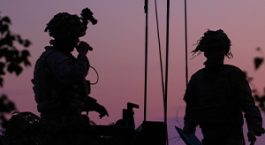 Silhouetted image of soldiers in a tropical locale attop an armored vehicle.