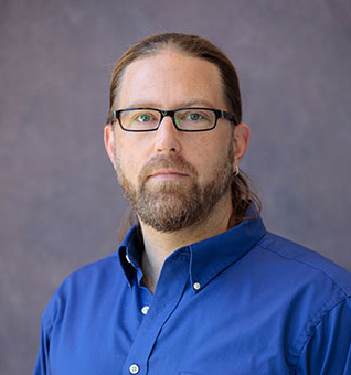 Photo of Erik Peterson in an oxford cloth shirt, wearing glasses and a beard.